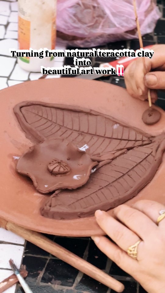 Hands adding fine clay details to a terracotta plate
